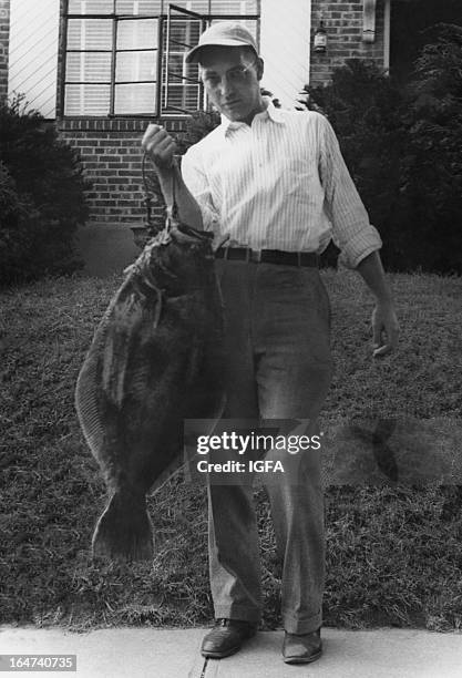 Man stands in front of a building holding a 20 pound summer flounder caught on 20 pound line in Oak Beach, New York on September 7, 1948.