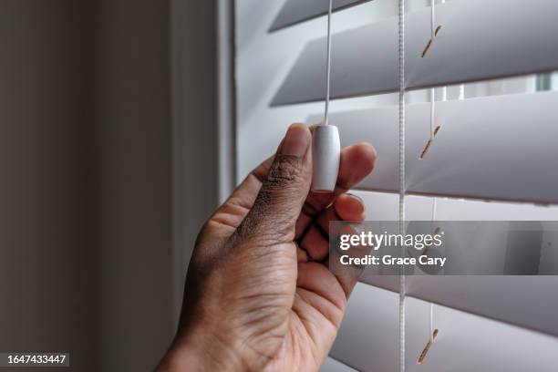 woman holds cord to open/close window blind - blinds stock pictures, royalty-free photos & images