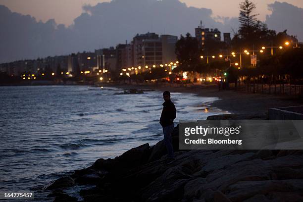 Man stands on rocks and looks out to sea at the illuminated waterfront in Limassol, Cyprus, on Wednesday, March 27, 2013. The ECB said on March 25 it...