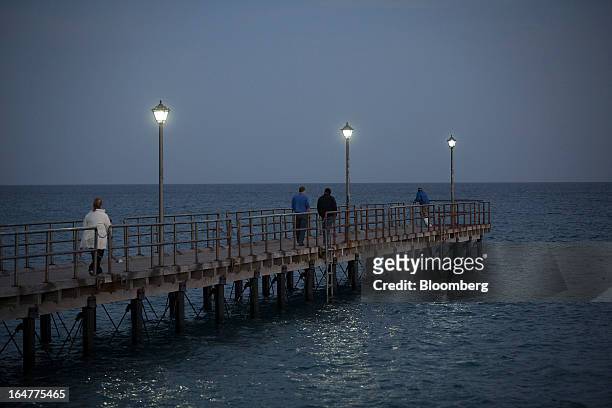 Tourists walk along a pontoon illuminated by electric lights on the waterfront in Limassol, Cyprus, on Wednesday, March 27, 2013. The ECB said on...