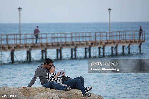 Couple sit on rocks and look out towards the Mediterranean sea in Limassol, Cyprus, on Wednesday, March 27, 2013. The ECB said on March 25 it won't...