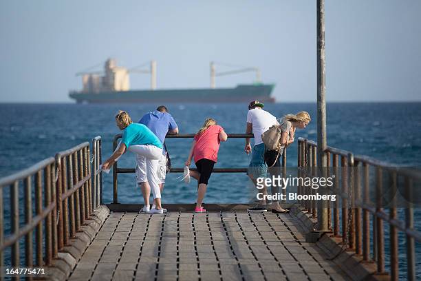 Tourists look out from a pontoon towards a commercial cargo ship in Limassol, Cyprus, on Wednesday, March 27, 2013. The ECB said on March 25 it won't...