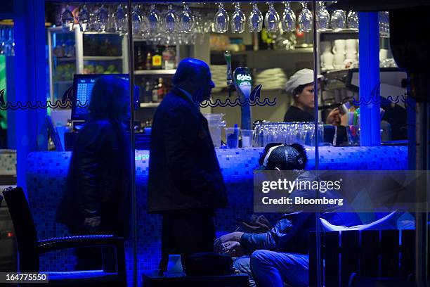 Customers are seen illuminated with blue light at a waterfront bar in Limassol, Cyprus, on Wednesday, March 27, 2013. The ECB said on March 25 it...