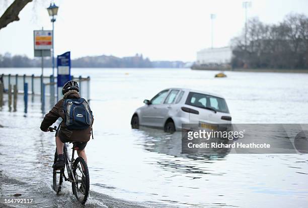 Cyclist rides past a car that is dissapearing beneth the incoming tide at the Putney Embankment on The River Thames on March 28, 2013 in London,...