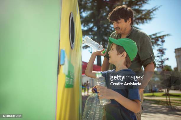 father teaching his little boy to recycle plastic waste using correct garbage bin at a city street - family decisions stock pictures, royalty-free photos & images
