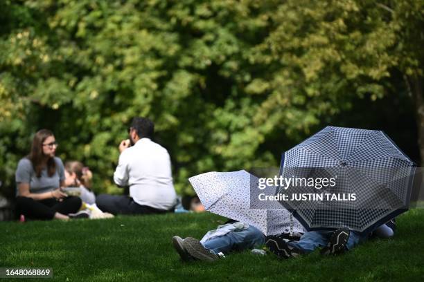 People take shelter from the sun under umbrellas while sunbathing in St James's Park in central London on September 6, 2023 as the late summer...