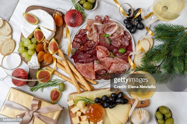 christmas appetizer table lunch meat italian prosciutto ham, parma ham, salami, bresaola beef and olives, cheese board and grissini breadstick. charcuterie plate. two glasses of white wine or prosecco and festive decor - apero noel photos et images de collection