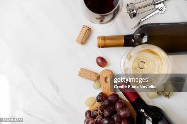 a glass of french white wine and a glass of red italian wine with wine bottles and grapes on a white table - elena collection fotografías e imágenes de stock