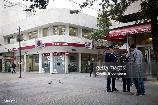 Police officers talk to a man outside a branch of Cyprus Popular Bank Pcl, also known as Laiki Bank, as banks open for the first time in two weeks in...