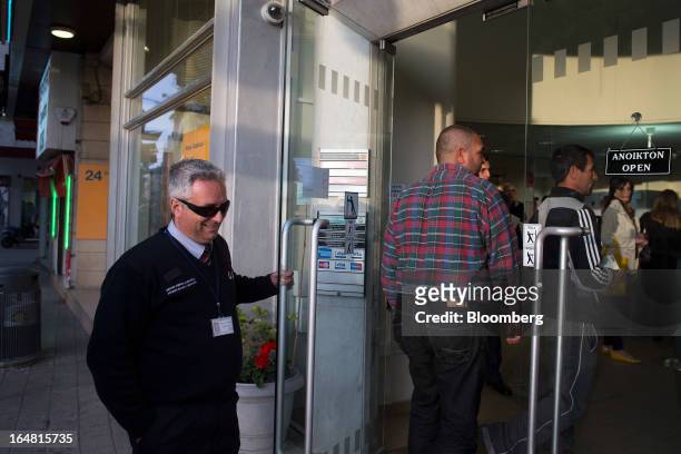 Security holds a door open for customers as they enter a Bank of Cyprus Plc branch. As banks open for the first time in two weeks in Nicosia, Cyprus,...