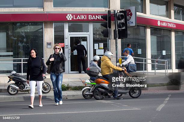 Pedestrians cross the road near a branch of Cyprus Popular Bank Pcl, also known as Laiki Bank, as banks open for the first time in two weeks in...