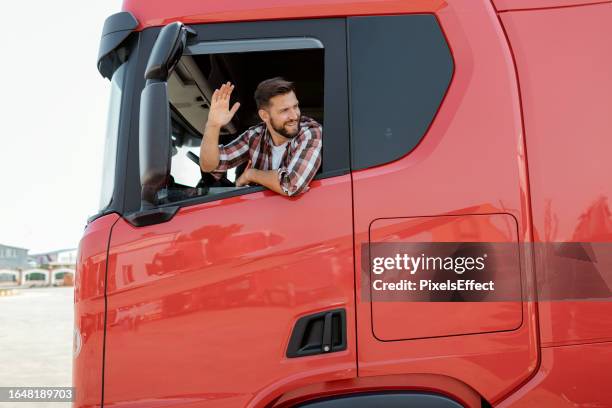 smiling male truck driver sitting inside truck and waving with his hand - truck driver stock pictures, royalty-free photos & images