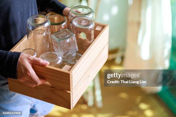 ausgeschnittenes bild der hände einer asiatischen frau, die leere gläser in eine holzkiste legt, die zum recycling bereit ist und einen nachhaltigen lebensstil zeigt. - einmachglas leer stock-fotos und bilder