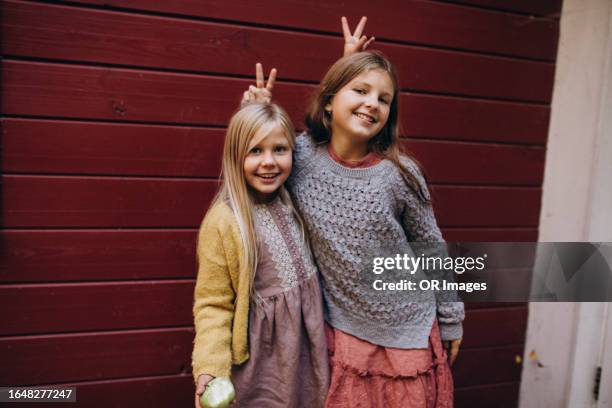 portrait of two happy playful girls at a wooden wall - sister stock pictures, royalty-free photos & images
