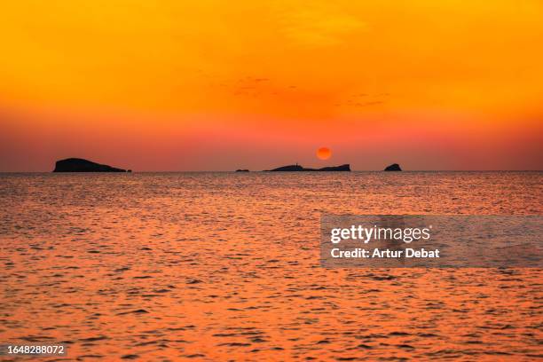red sun disk setting above the horizon from the cala comte in the ibiza island. - sun ibiza stock-fotos und bilder