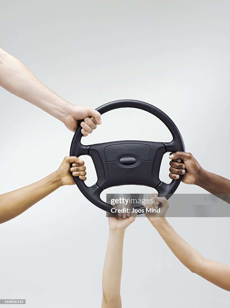 Multiple hands holding a car steering wheel