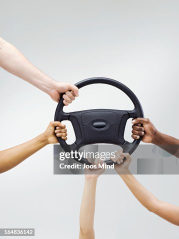 Multiple hands holding a car steering wheel Multiple hands holding a car steering wheel