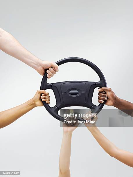 multiple hands holding a car steering wheel - steering wheel stock pictures, royalty-free photos & images