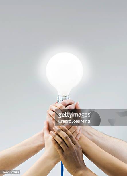 hands holding a large light bulb - zusammenhalt stock-fotos und bilder