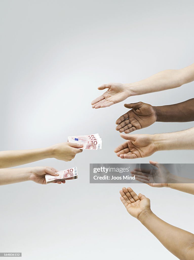 Hand holding out money, multiple hands receiving