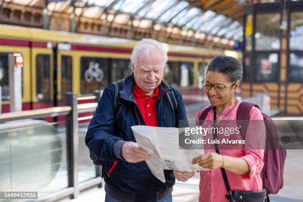 senior couple  on vacation standing at railway station in the city and looking at a map - berlin map stock pictures, royalty-free photos & images