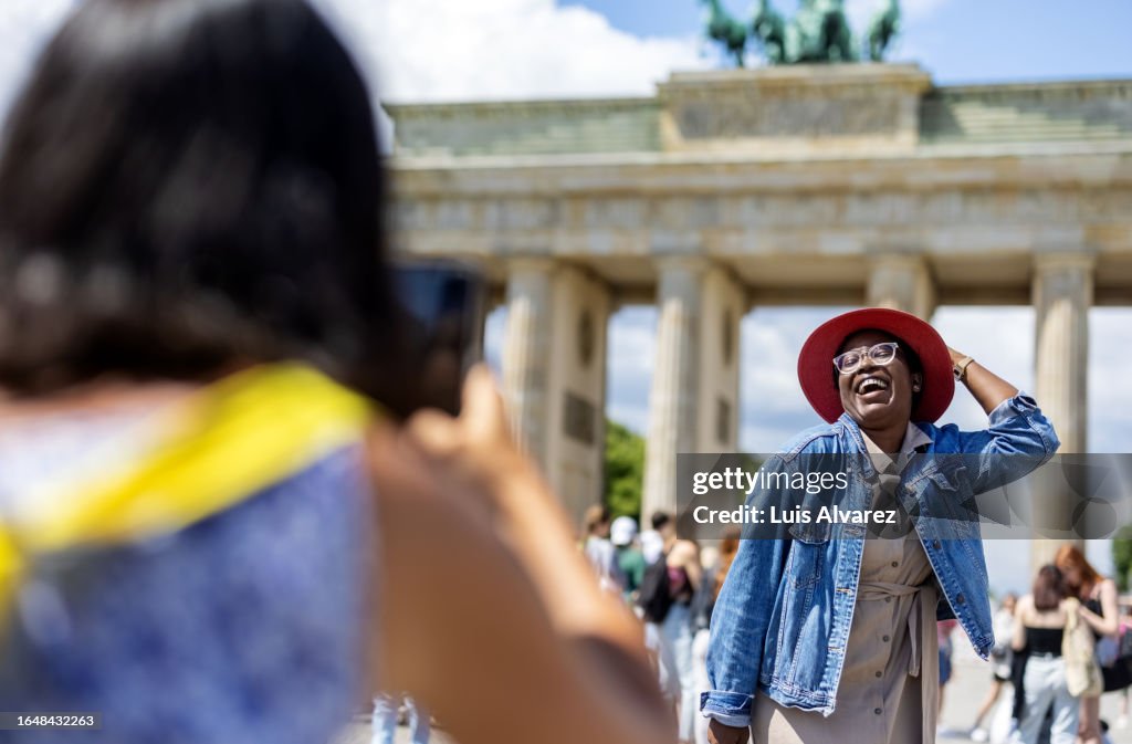 African woman standing in front of Brandenburg Gate being photographed by her friend