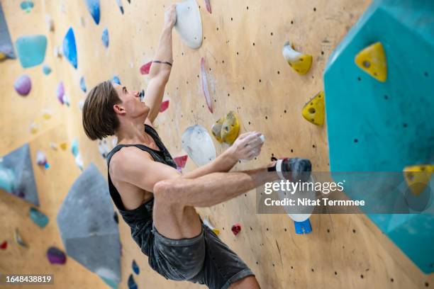 exercise can improve your health and physical ability. side view of a male climber gripping and climbing a bouldering wall in an indoor climbing gym. - chalk wall stock pictures, royalty-free photos & images