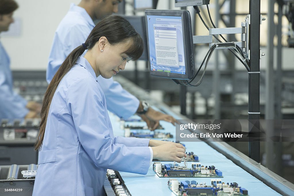 Woman works on circuit board on conveyor belt