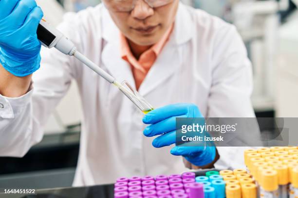 midsection of female medical healthcare worker filling chemical in tray using pipette while working in laboratory - microplate stock pictures, royalty-free photos & images