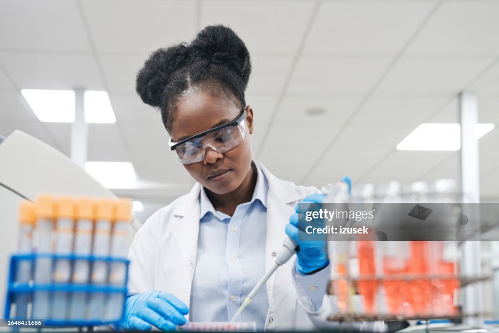 Young female scientist filling chemical through pipette while working in laboratory