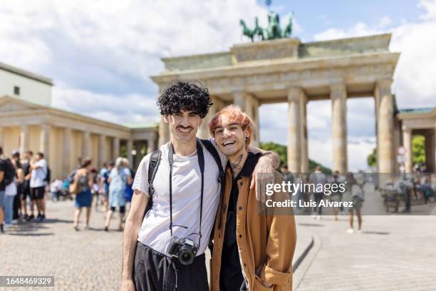 portrait of happy gay couple standing together in front of brandenburg gate - voyageur homme devant monument photos et images de collection