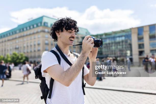 happy young traveller taking photo using his camera on vacation. - spiegelreflexkamera stock-fotos und bilder