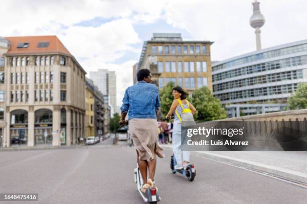 two women travellers enjoying riding e-bike in a foreign city - berlin diversity alexanderplatz stockfoto's en -beelden