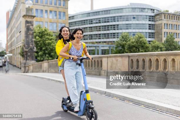 portrait of two cheerful women friends on holiday having fun on push scooter in city - trotinete imagens e fotografias de stock