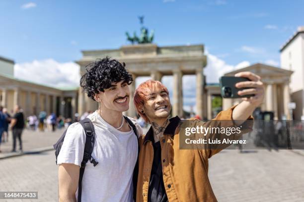 gay couple on vacation taking selfie in front of brandenburg gate in berlin - voyageur homme devant monument photos et images de collection