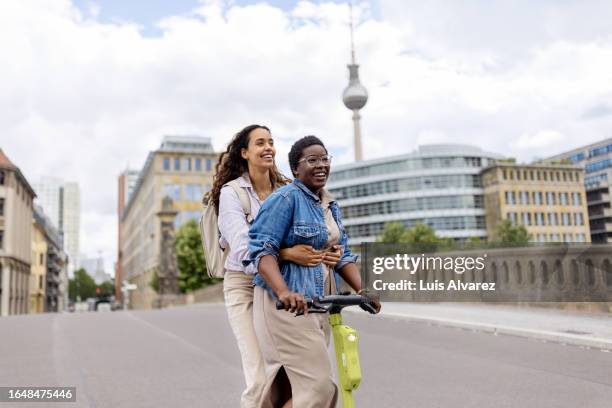 two young women travellers riding on an electric push scooter on vacation - berlin diversity alexanderplatz stockfoto's en -beelden