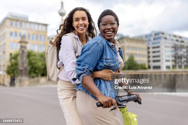 two diverse women friends messing around in a city on electric scooter - berlin diversity alexanderplatz stockfoto's en -beelden