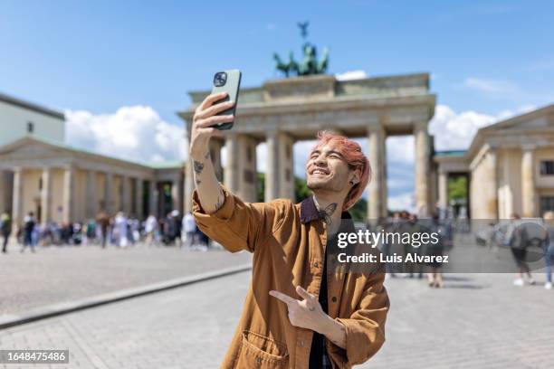 handsome young man taking selfie in front of brandenburg gate - voyageur homme devant monument photos et images de collection