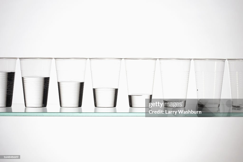 A row of glasses with varying amounts of water descending from full to empty