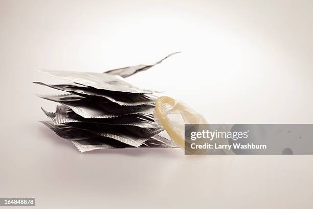 several unopened condom wrappers in a stack and one opened one - condom stock pictures, royalty-free photos & images