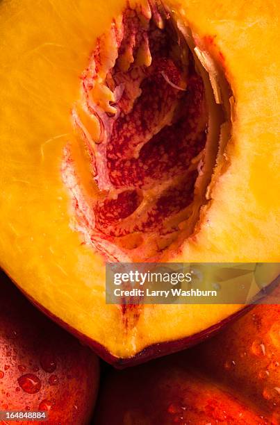 half of a juicy peach resting on two uncut peaches, full frame - peach stockfoto's en -beelden