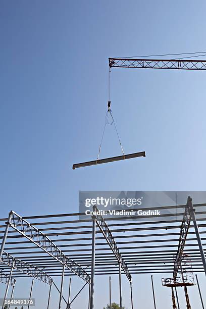 crane lowering steel beam towards construction frame - crane construction machinery stock pictures, royalty-free photos & images