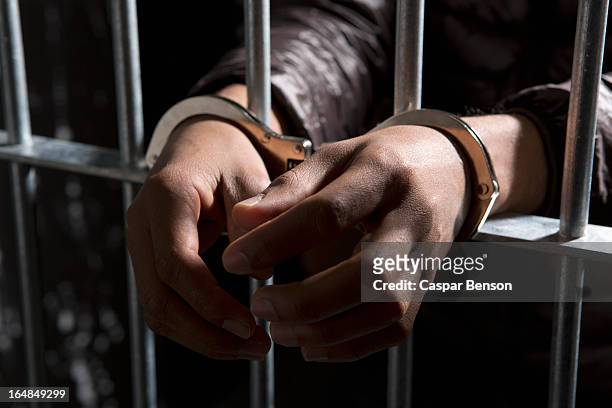 a prisoner behind bars with hands cuffed - häftling stock-fotos und bilder