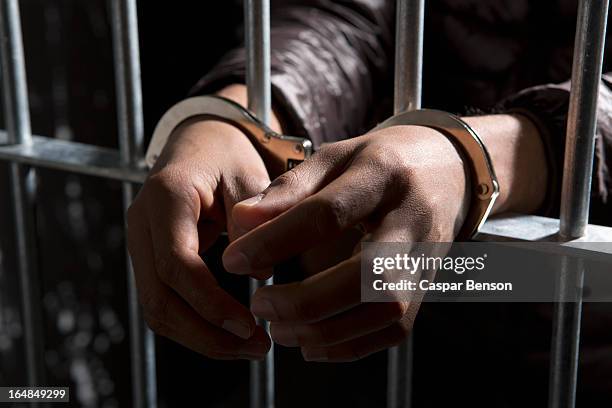 a prisoner behind bars with hands cuffed - cárcel fotografías e imágenes de stock