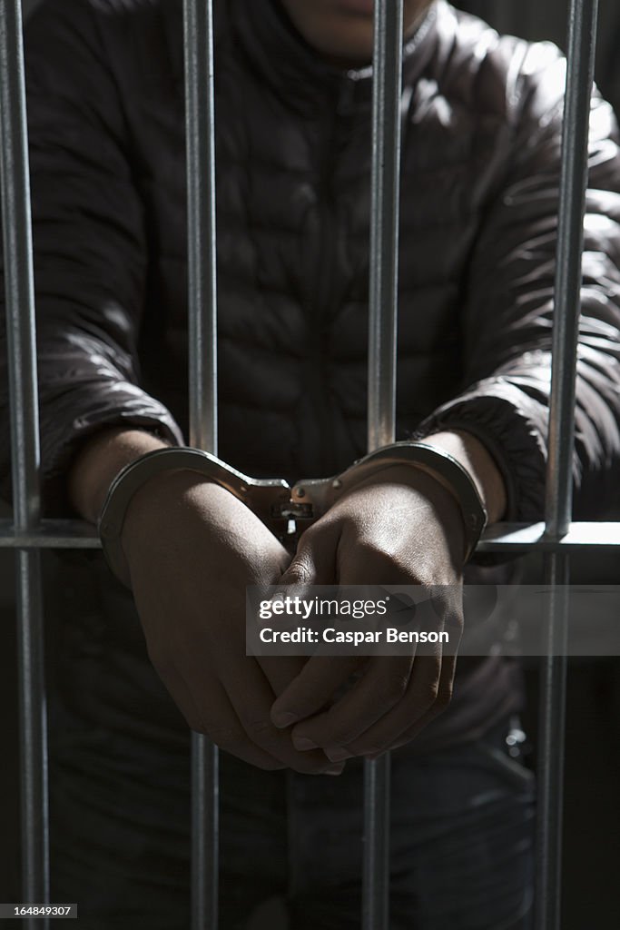 A prisoner behind bars with hands cuffed