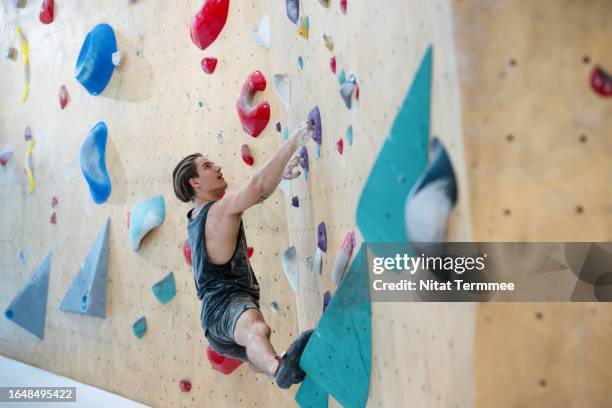 dose indoor climbing at a wall to improve your physical fitness and mental health. young male athlete climbing and grip following a route on a climbing wall in the indoor climbing gym. - parete rocciosa foto e immagini stock