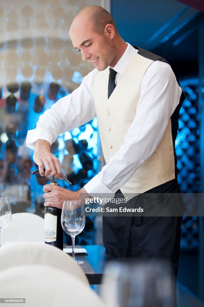 Empregado de Mesa uncorking garrafa de vinho no restaurante