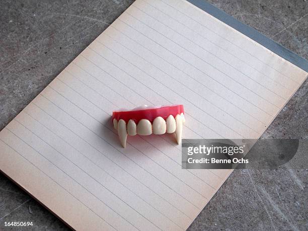 a set of vampire fangs on top of a note pad of lined paper - vampir stock-fotos und bilder