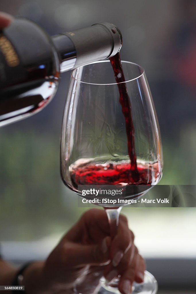 A woman pouring a sampling of red wine at a wine tasting, focus on hands