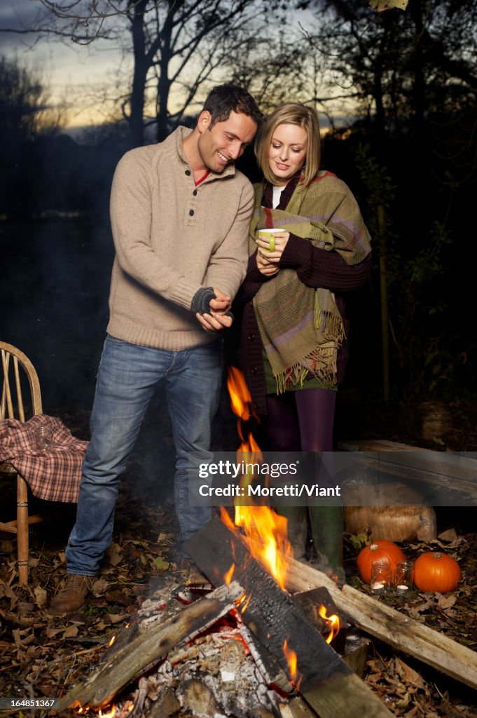 Casal relaxante por Fogueira de acampamento ao pôr do sol
